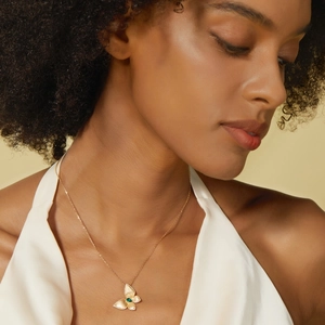 Détail macro d'un collier papillon en or brossé avec pendentif émeraude porté par un modèle