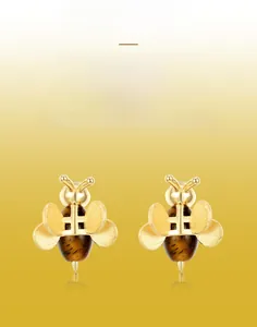 Gros plan de boucles d'oreilles abeilles dorées avec texture brossée et pierre œil-de-tigre