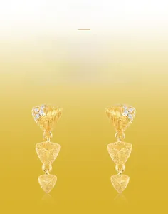 Macro view of handmade brushed S925 gold earrings featuring heart and triangle pendants