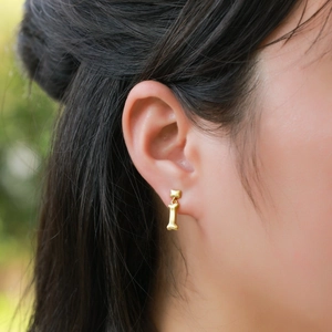 Primo piano di orecchini a forma di osso in oro spazzolato indossati da una modella