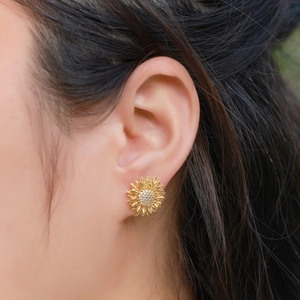 Macro shot of asymmetric sunflower stud earring with gold finish and sparkling zircons