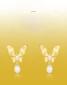 Detailed macro view of gold butterfly earrings with brushed metal finish and pearl drops
