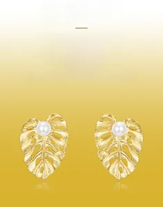 Detail of leaf-shaped earrings with brushed gold texture and white pearl accents