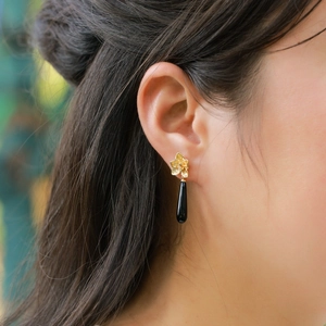 Elegant gold flower drop earrings with black onyx teardrop pendant on female model
