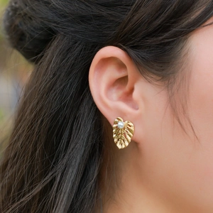 Close-up of golden monstera leaf earring with brushed metal texture and pearl accent