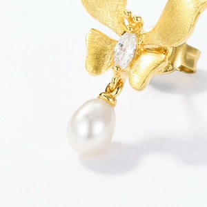 Brushed gold butterfly earrings with marquise crystal and drop pearl on white background