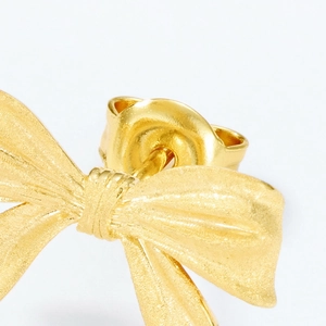 Close-up of matte gold bow earring featuring a fine brushed metallic texture and detail