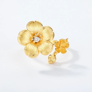 Golden flower ring with brushed texture and sparkling center stone on white background