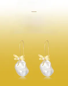 Detail of golden brushed dragonfly earrings featuring a white baroque pearl drop charm
