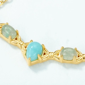 Macro detail of V-shaped gold necklace with teardrop amazonite and green gemstones