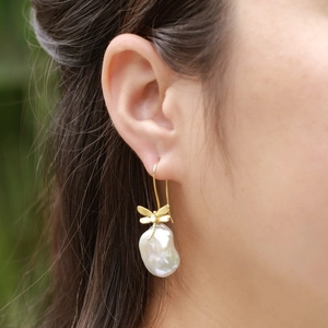 Elegant gold dragonfly earrings with baroque pearl drops worn on a female model