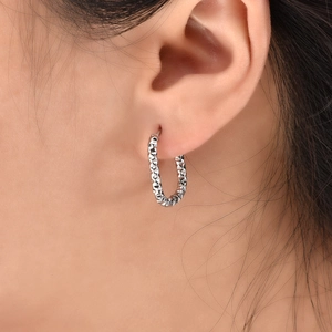 Close-up of a silver U-shaped hoop earring with a diamond-cut textured surface on an ear
