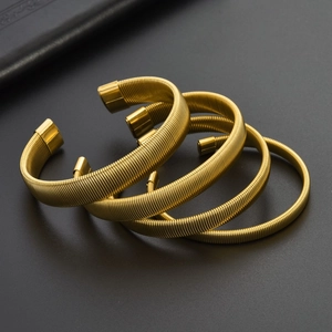 Set of four gold 18K flexible C-shaped bracelets with spiral texture on black background