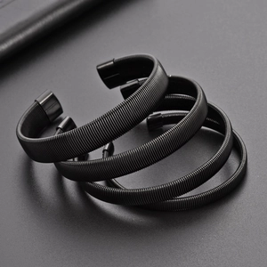 Close-up of four matte black elastic metal spring armbands on a textured gray background