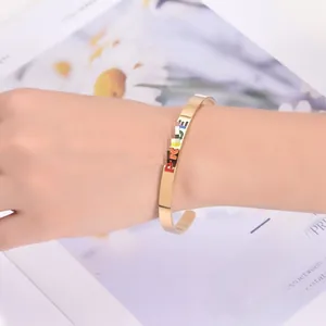 Detail of gold C-shaped stainless steel cuff bracelet featuring rainbow Pride lettering