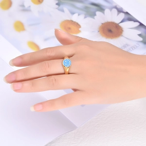 Close-up of a minimalist gold ring with a blue smiley face emoji on a model's finger