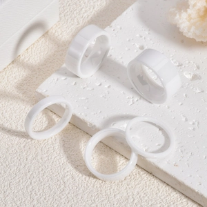 Minimalist white ceramic rings in varying widths displayed on a textured stone surface