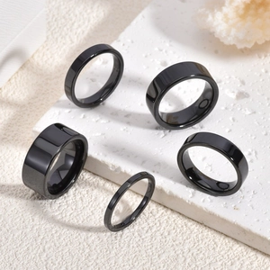 Set of five polished black ceramic rings in various widths displayed on a stone surface