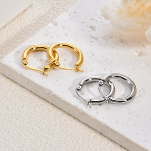 Détail de boucles d'oreilles créoles polies en or et argent sur un socle en pierre
