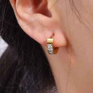 Gros plan d'un modèle portant des boucles d'oreilles huggie en acier doré et zircons