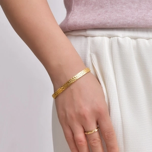Détail d'un bracelet jonc doré en forme de C avec texture écaillée porté avec une bague