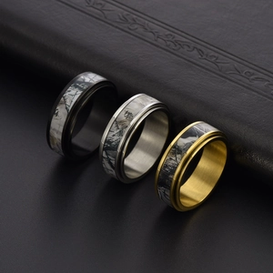Detail of three rotating stainless steel rings with camouflage branch inlay in black, gold and silver