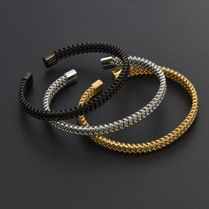 Detailed view of three braided stainless steel open bangles in black, silver and gold finish