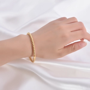 Detail view of a 18K gold-plated beaded bracelet worn on a wrist over white silk