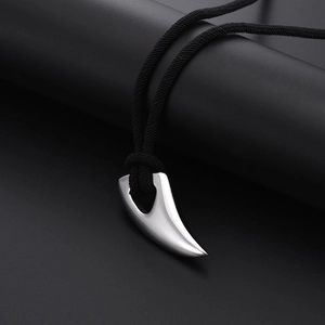 Polished stainless steel wolf tooth pendant with black braided cord on dark background