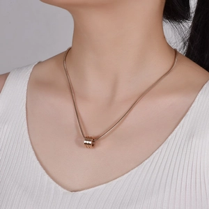 Detail of rose gold cylinder pendant necklace on model with sleek snake chain link