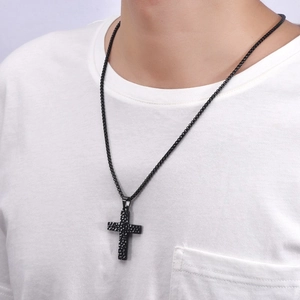 Close-up of men's black hammered cross pendant on a thin chain over a white t-shirt