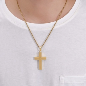 Close-up of golden cross pendant necklace with engraved texture on a white t-shirt