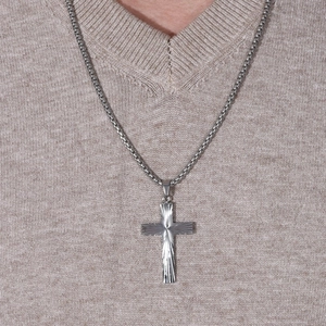 Gros plan du pendentif croix argenté avec gravure solaire sur une chaîne à mailles carrées
