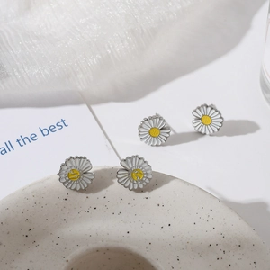 Minimalist daisy stud earrings with white petals and yellow centers in a lifestyle setting