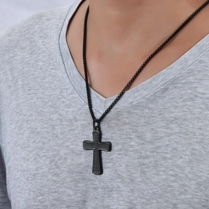 Détail d'un pendentif croix hip-hop noir texturé porté sur une chaîne à billes noire