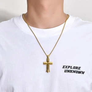 Detail of a vintage embossed gold cross pendant on a thin chain worn with a white T-shirt