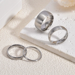 Minimalist matte brushed stainless steel rings in various widths on a stone display