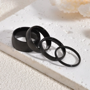 Set of four black brushed titanium steel rings in various widths on a textured stone