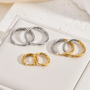 Three pairs of twisted hoop earrings in gold, silver, and two-tone finishes displayed on stone