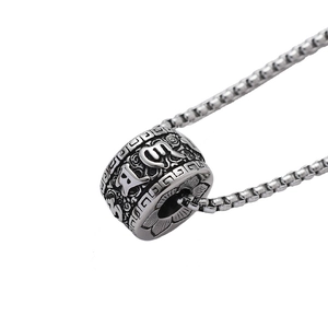 Macro shot of stainless steel cylinder pendant with six-word mantra and lotus engraving