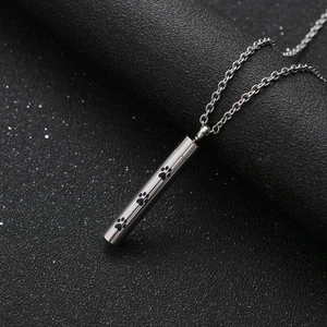 Pendentif cylindre en acier inoxydable pour cendres avec empreintes de pattes sur fond noir