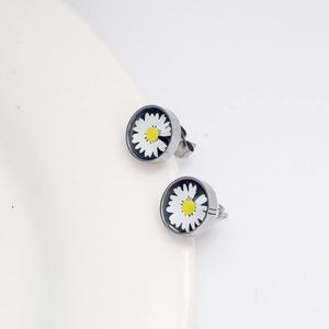 Détails des boucles d'oreilles marguerites avec pétales blancs sur une assiette en céramique