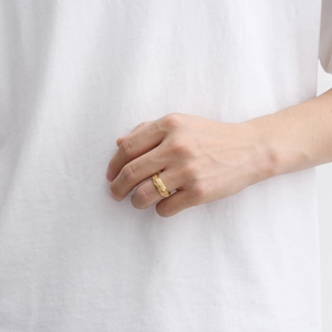 Detail of a wide gold spinning ring featuring embossed ancient mantra patterns on the finger