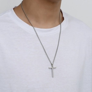 Close-up of polished stainless steel cross pendant worn over a white T-shirt