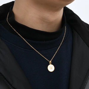 Close-up of a gold necklace featuring a round pendant with the letter W on a model