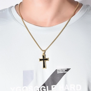 Close-up of a gold cross pendant with black enamel inlay worn on a model over a grey tee