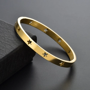 Close-up of polished gold steel bracelet with hollow star cutouts on black gift box