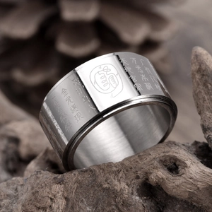 Rotating stainless steel religious ring with engraved mantra on natural wood background