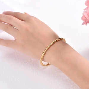 Detail view of 18K gold bamboo joint bracelet on a wrist with floral decoration