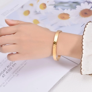 Detail of handmade hammered texture on gold-plated open cuff bracelet worn on a wrist